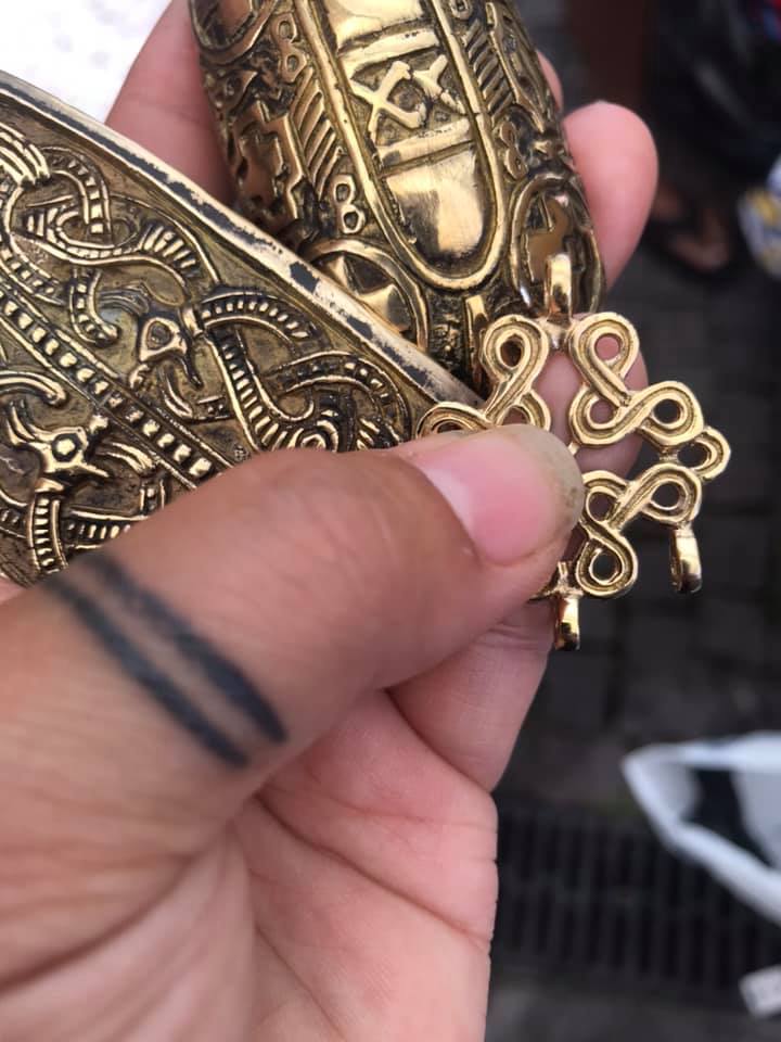 Närbild av hand som håller en pärlspridare och en halsbandsbuckla i vikingainspirerad metall.