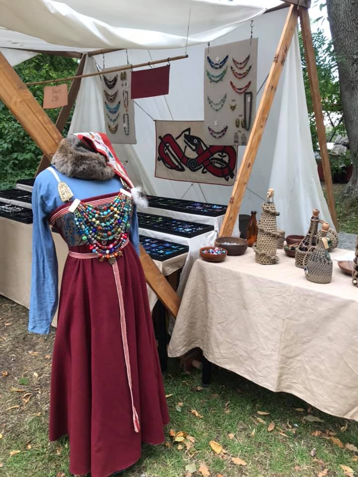 Vikingainspirerad dräkt med rikt pärlhalsband, uppställd i marknadsstånd på medeltidsmarknad.
