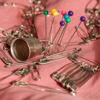 Knappnålar, säkerhetsnålar och fingerborg utspridda på tyg